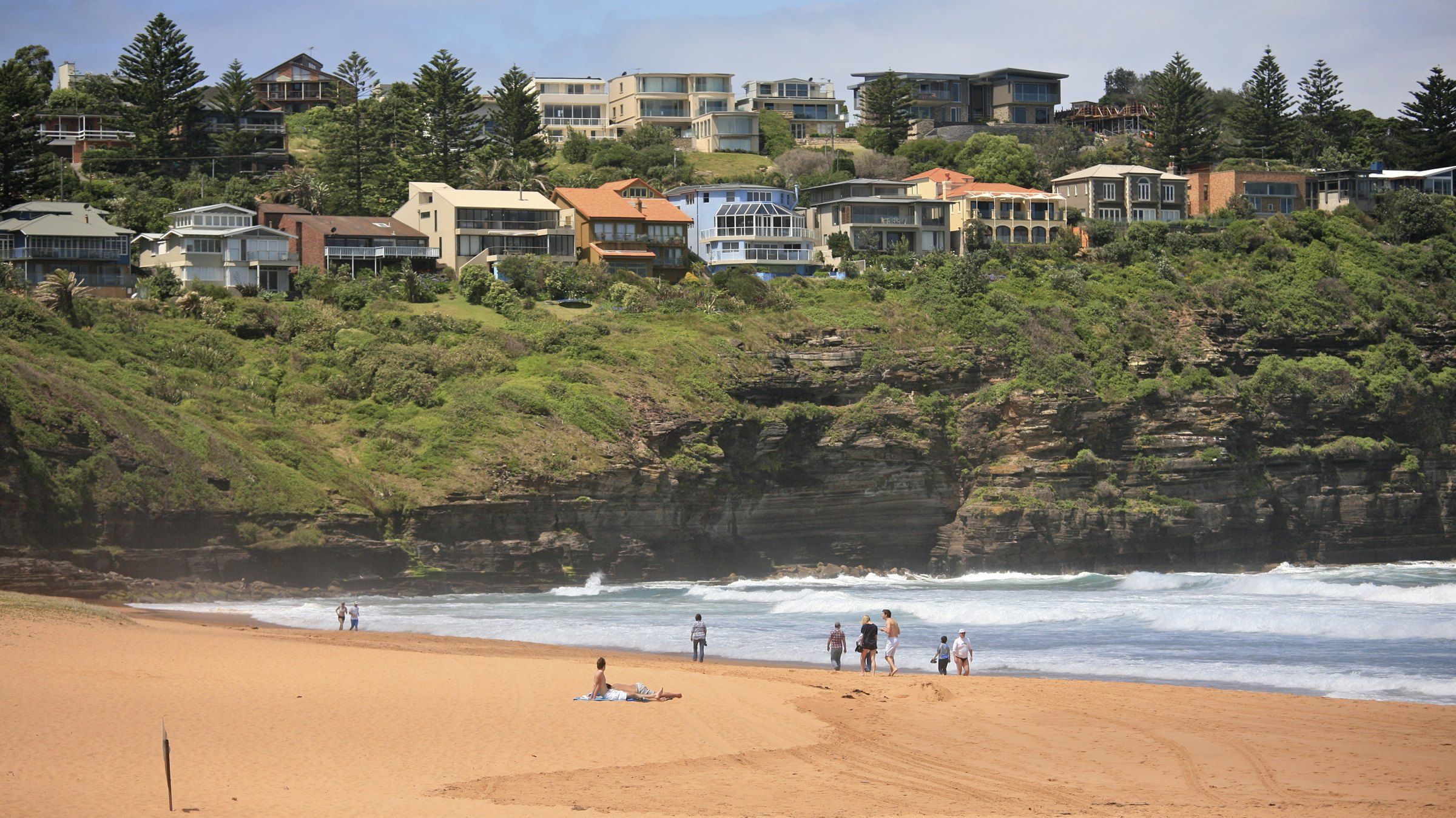 Houses on the slope above Bilgola Beach, a few people on the sand below