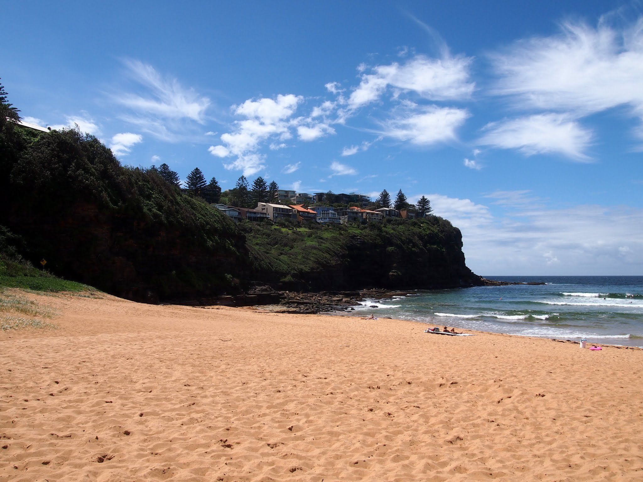 Bilgola Beach on a sunny day: wide sand, the bush-covered headland and clear surf