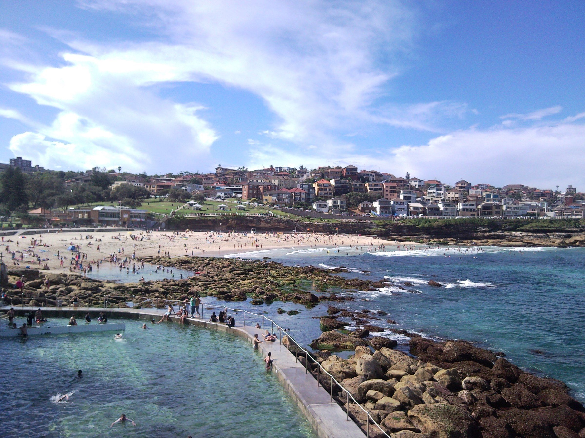 Bronte Beach on a sunny afternoon, the ocean pool on the rocks in front and houses on the hill behind