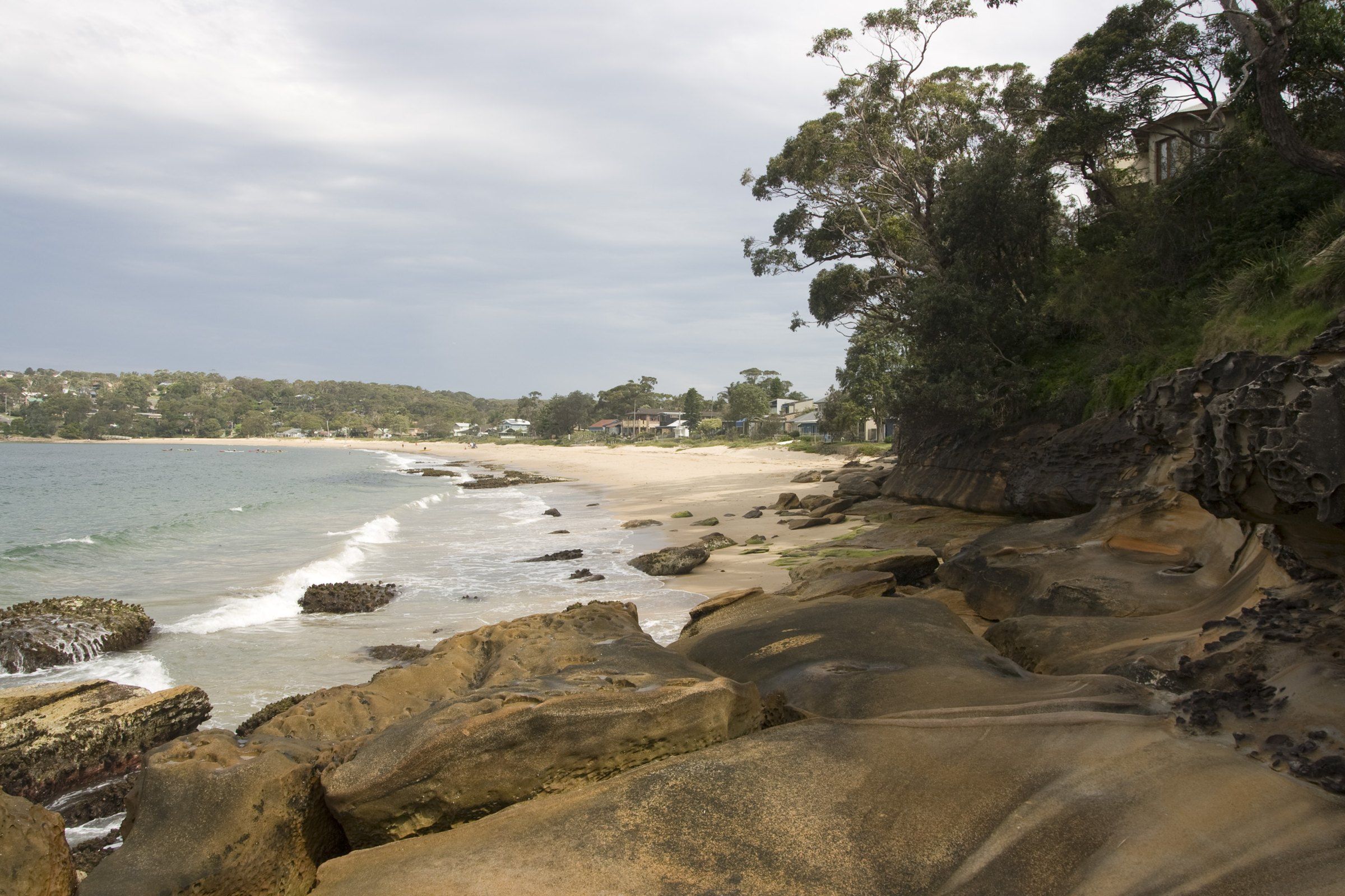 Horderns Beach at Bundeena seen past sandstone rocks, calm water and houses beyond