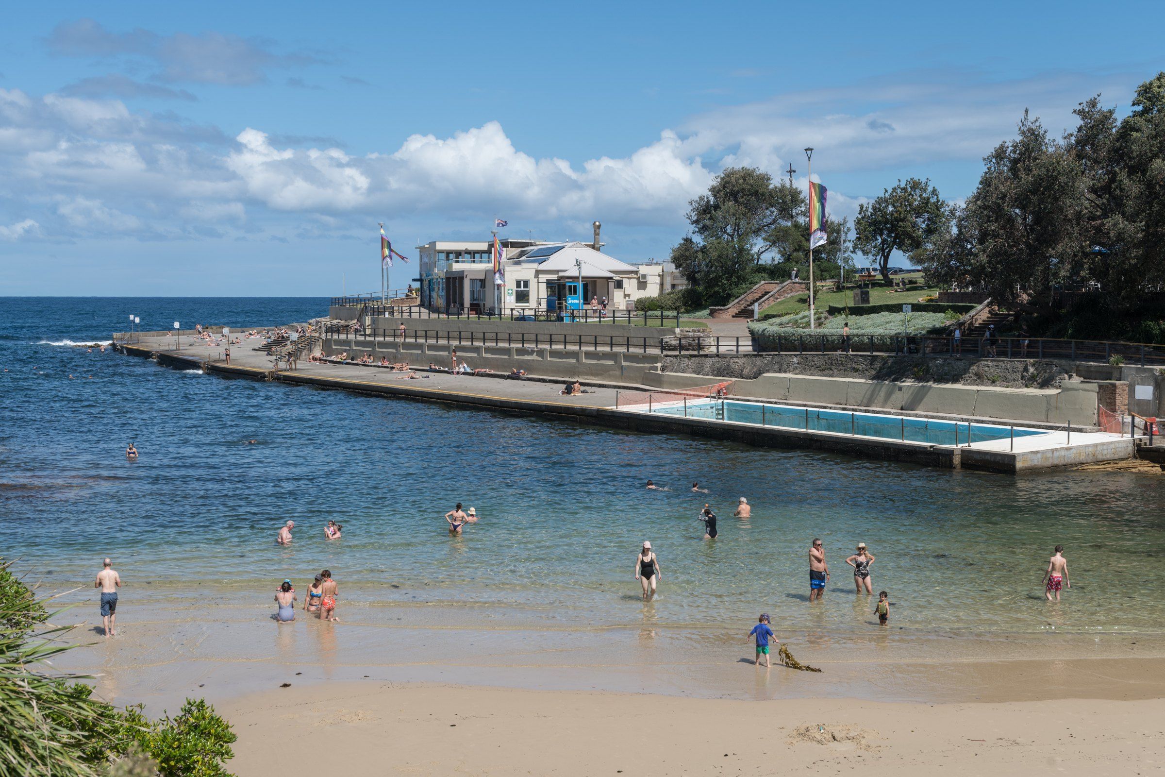 Clovelly Beach on a sunny day, swimmers in the calm bay and the concrete promenade along the side