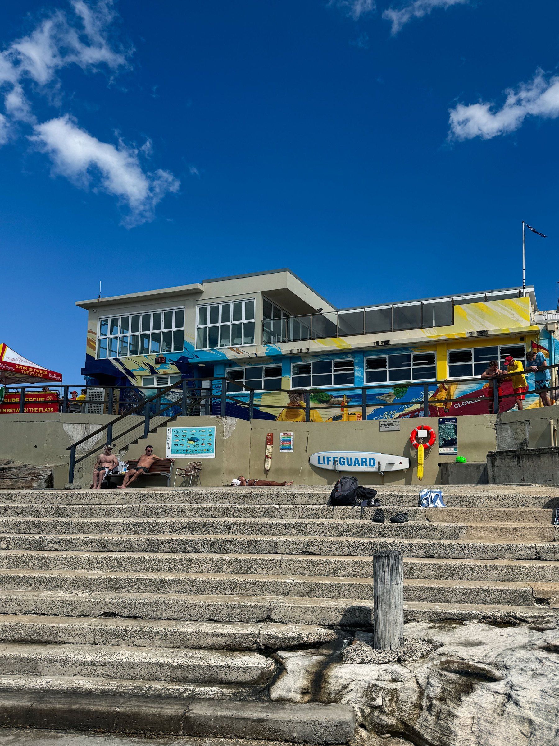 The Clovelly surf club building and steps above the beach under a blue sky