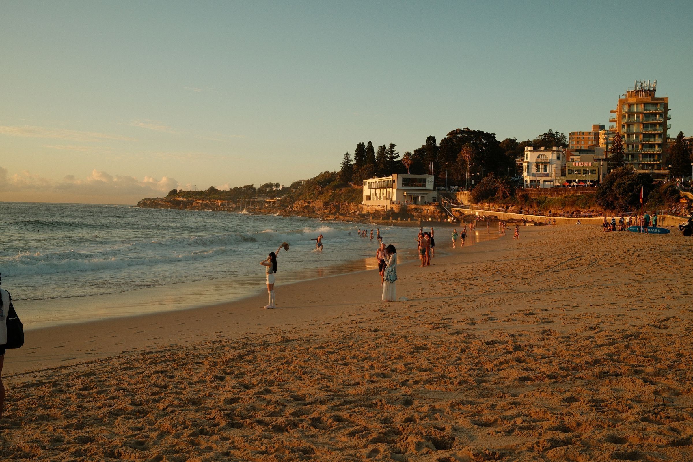 Coogee Beach in late-afternoon light, swimmers in the surf and the surf club on the southern headland
