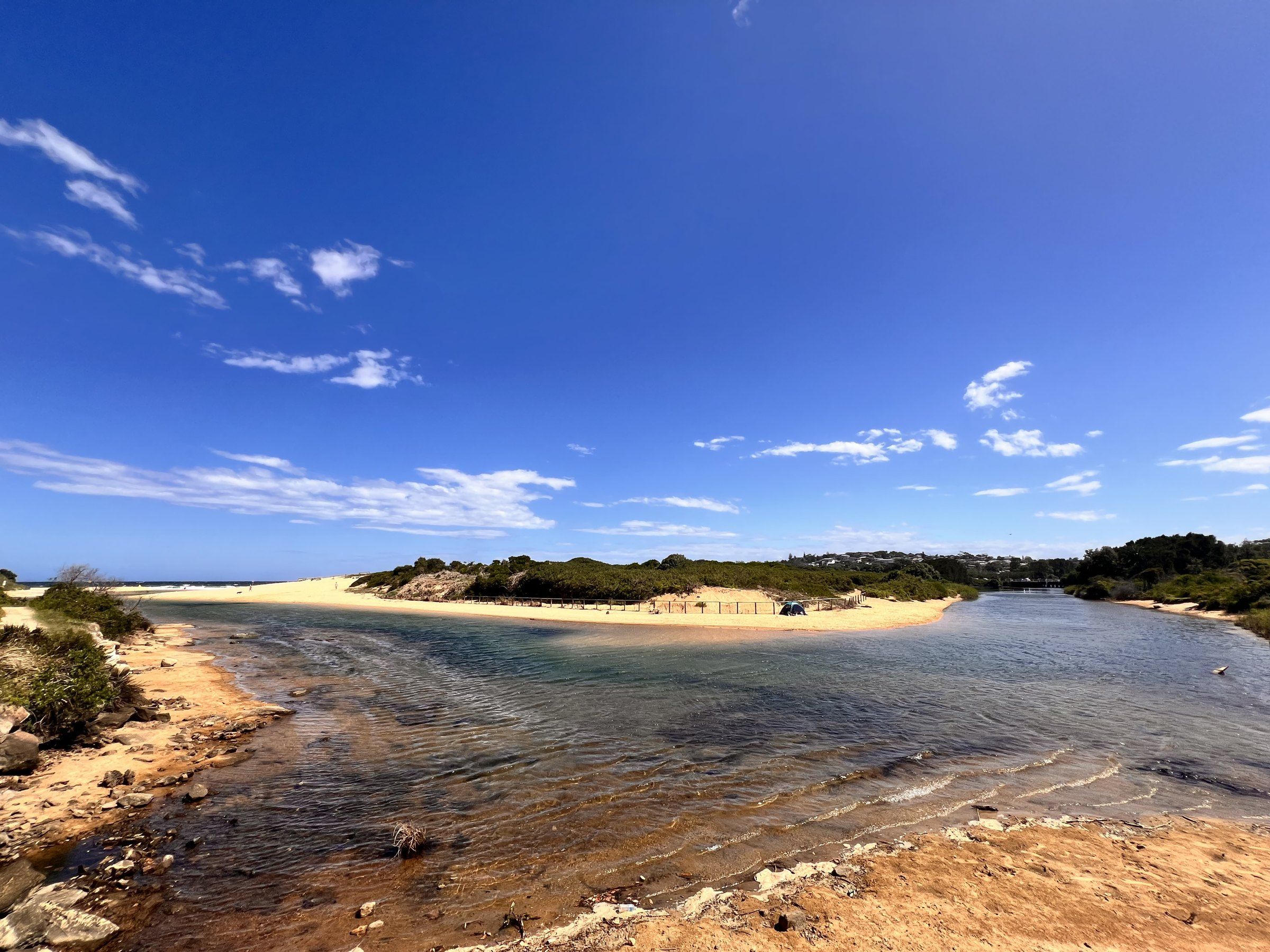 Curl Curl Lagoon running across the sand towards the sea under a blue sky