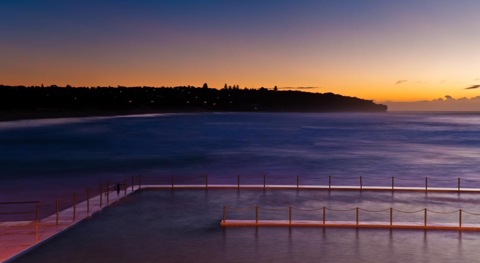 The North Curl Curl rock pool at sunrise, the headland dark against an orange sky