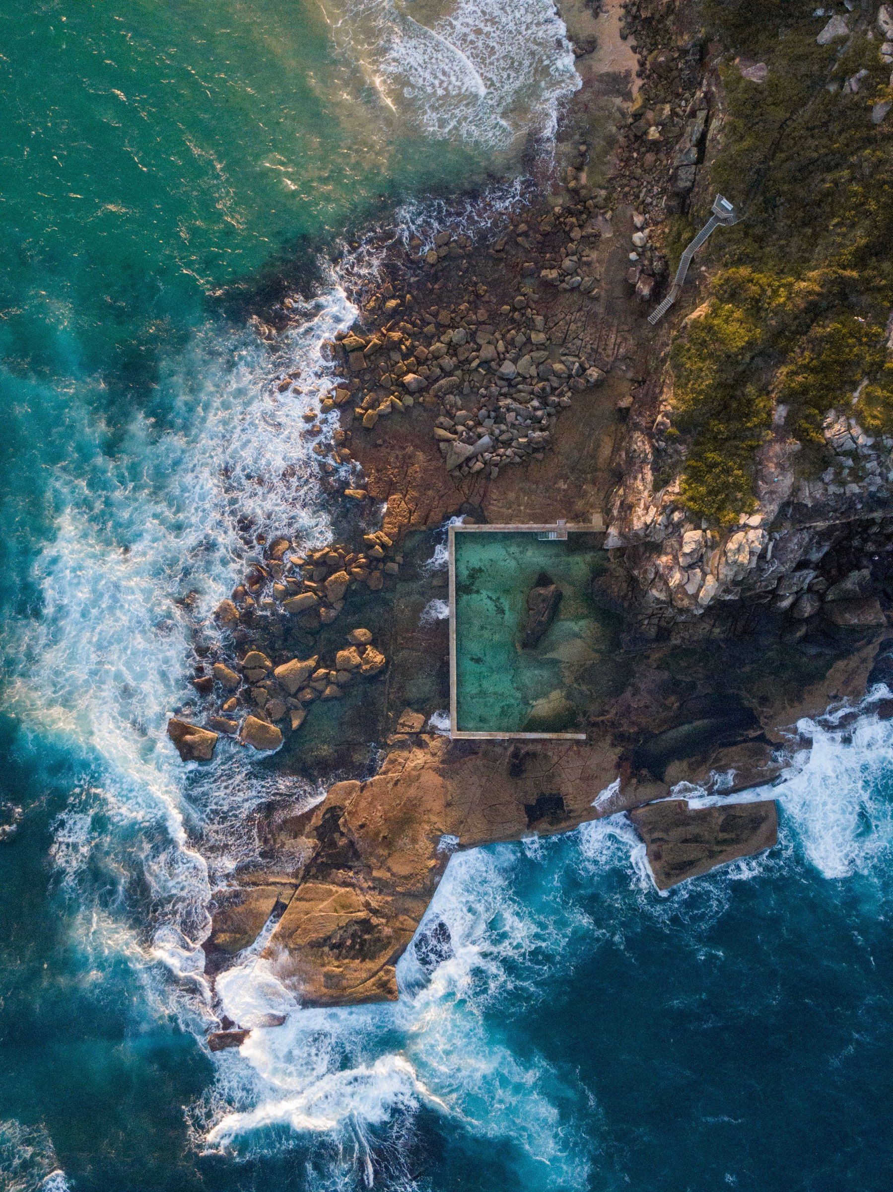 A Curl Curl rock pool from above, cut into the rock platform with waves breaking around it