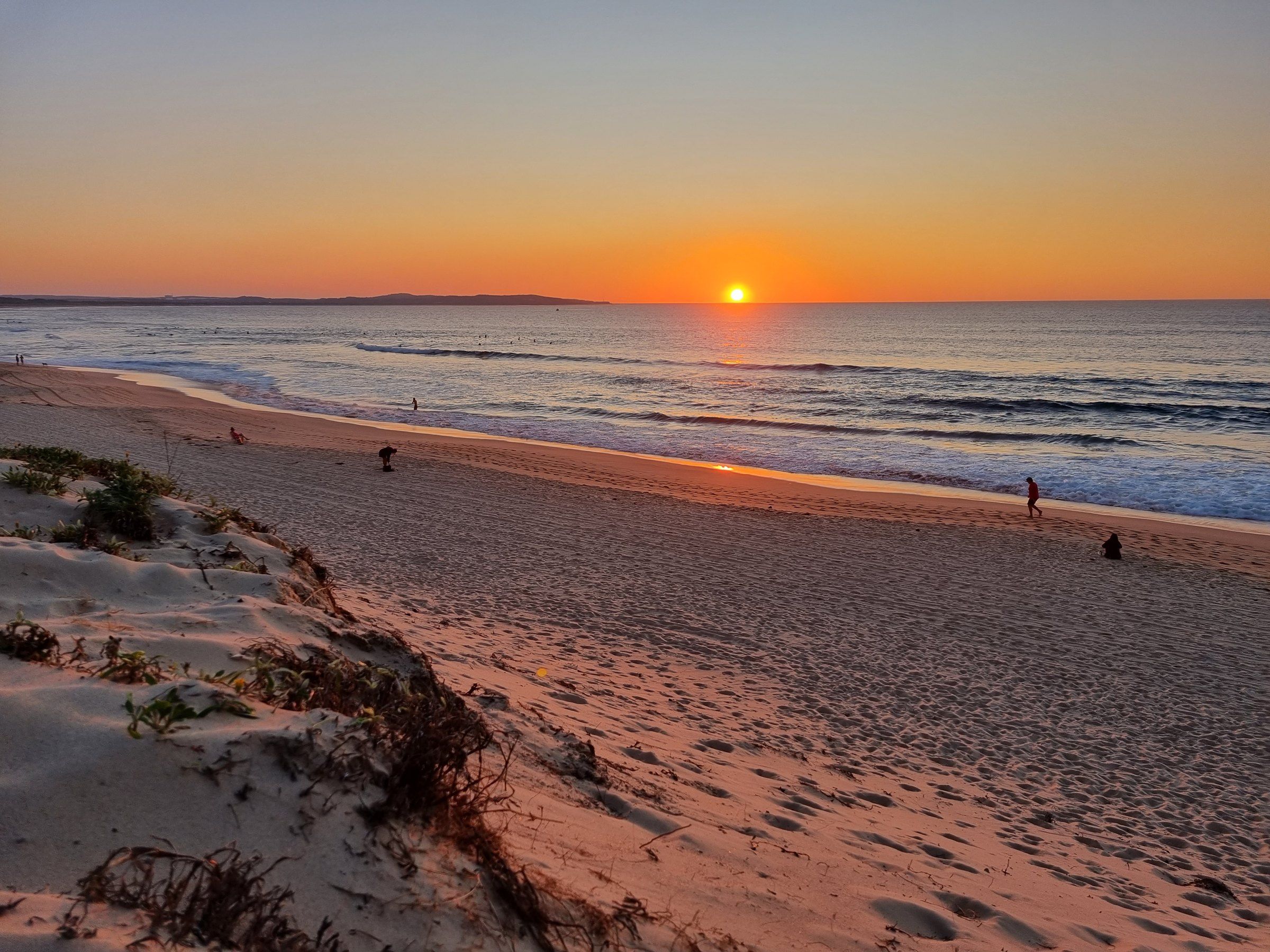 The sun rising over the ocean at Elouera Beach, the sand still in shadow