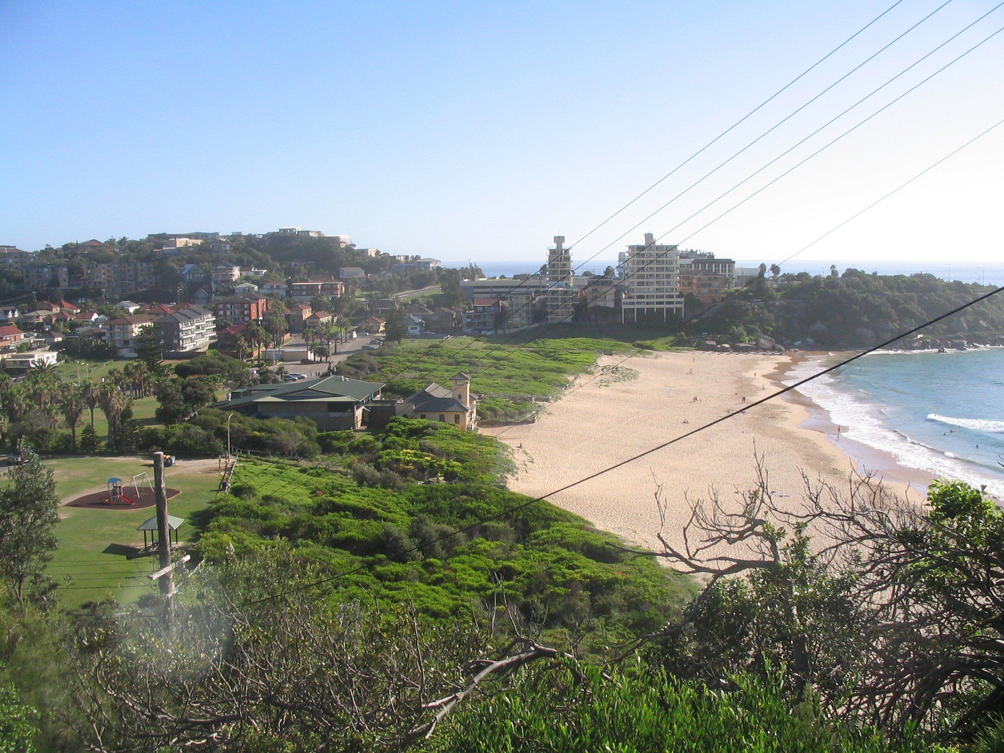 Freshwater Beach seen from the headland on a sunny day, the sand below the houses and the next headland beyond