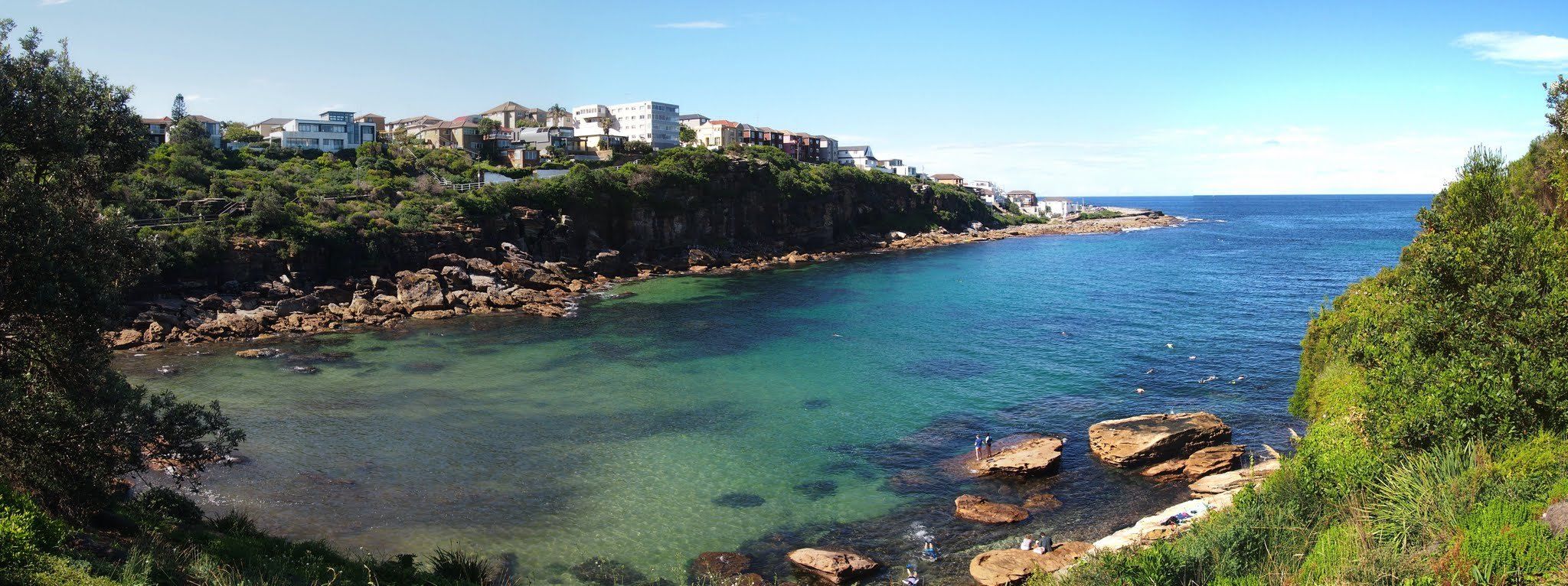 Gordons Bay from the bush above, green water inside the cove and houses on the headland