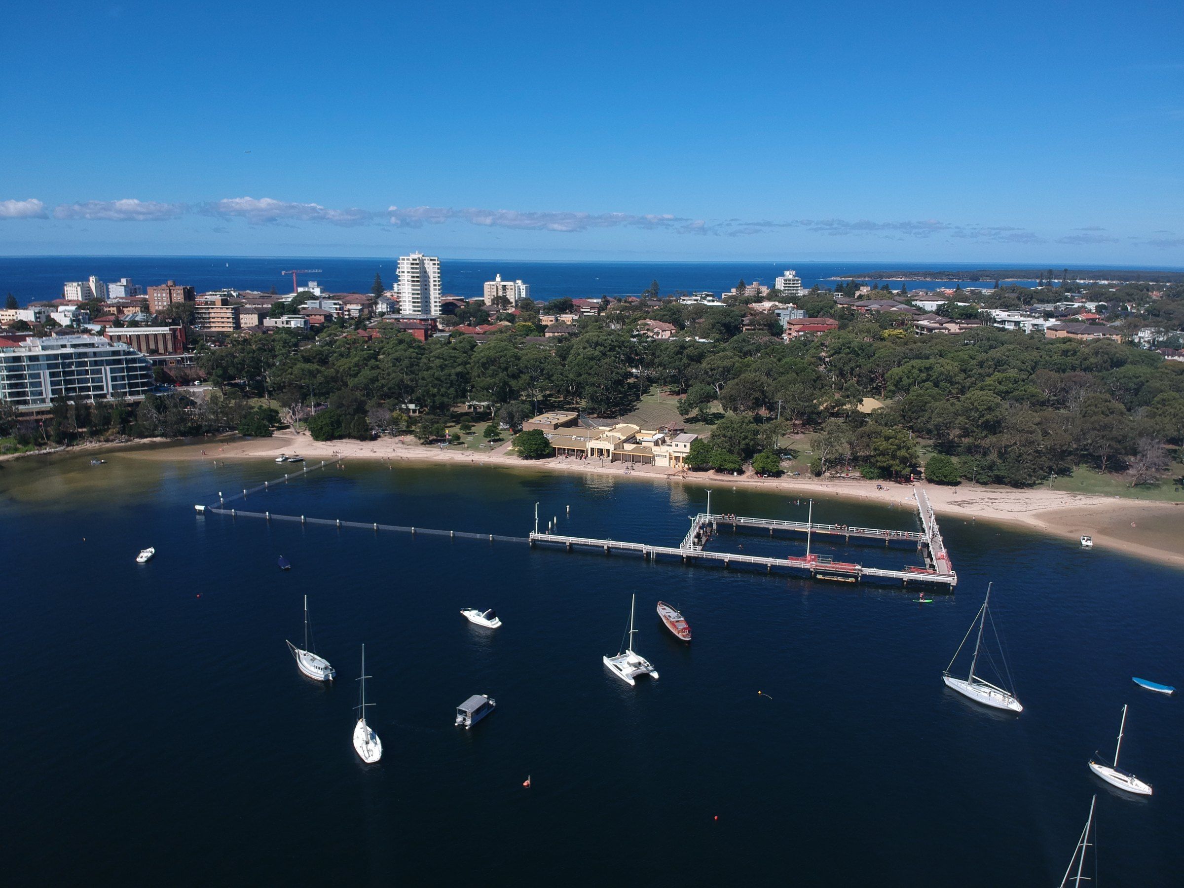 The netted Gunnamatta Bay baths from above, with yachts moored in the bay and Cronulla behind