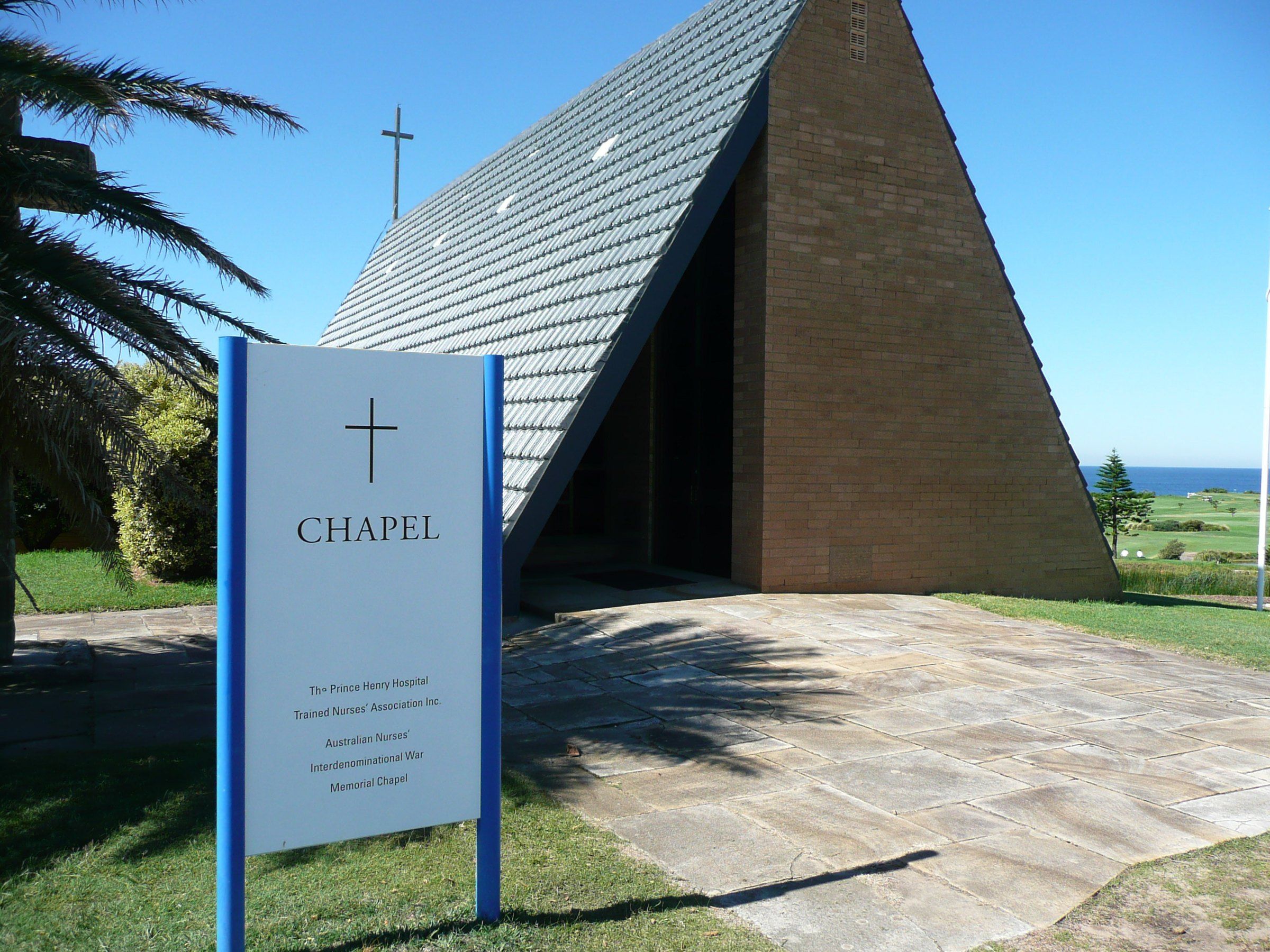 The steep-roofed War Memorial Chapel at Prince Henry, Little Bay, with its sign in front