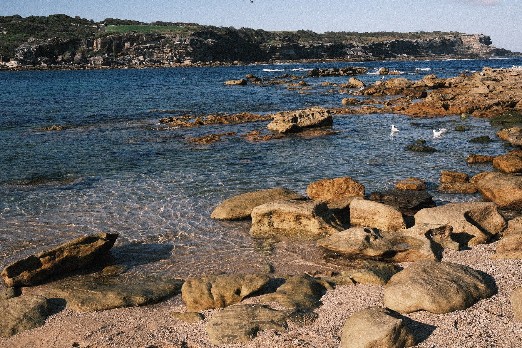 Sandstone boulders and rock ledges at the edge of Little Bay, calm water beyond