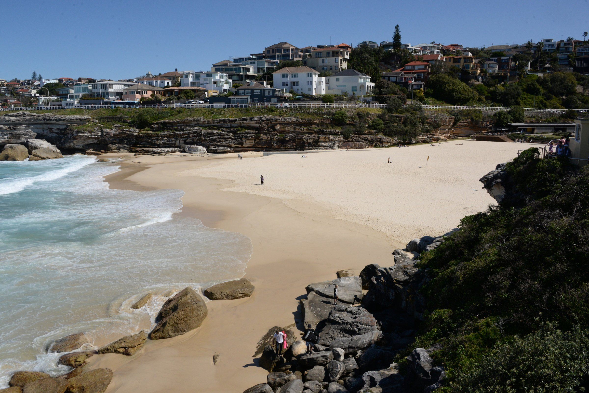 The sand and rocks at Tamarama on a clear day, houses above the beach