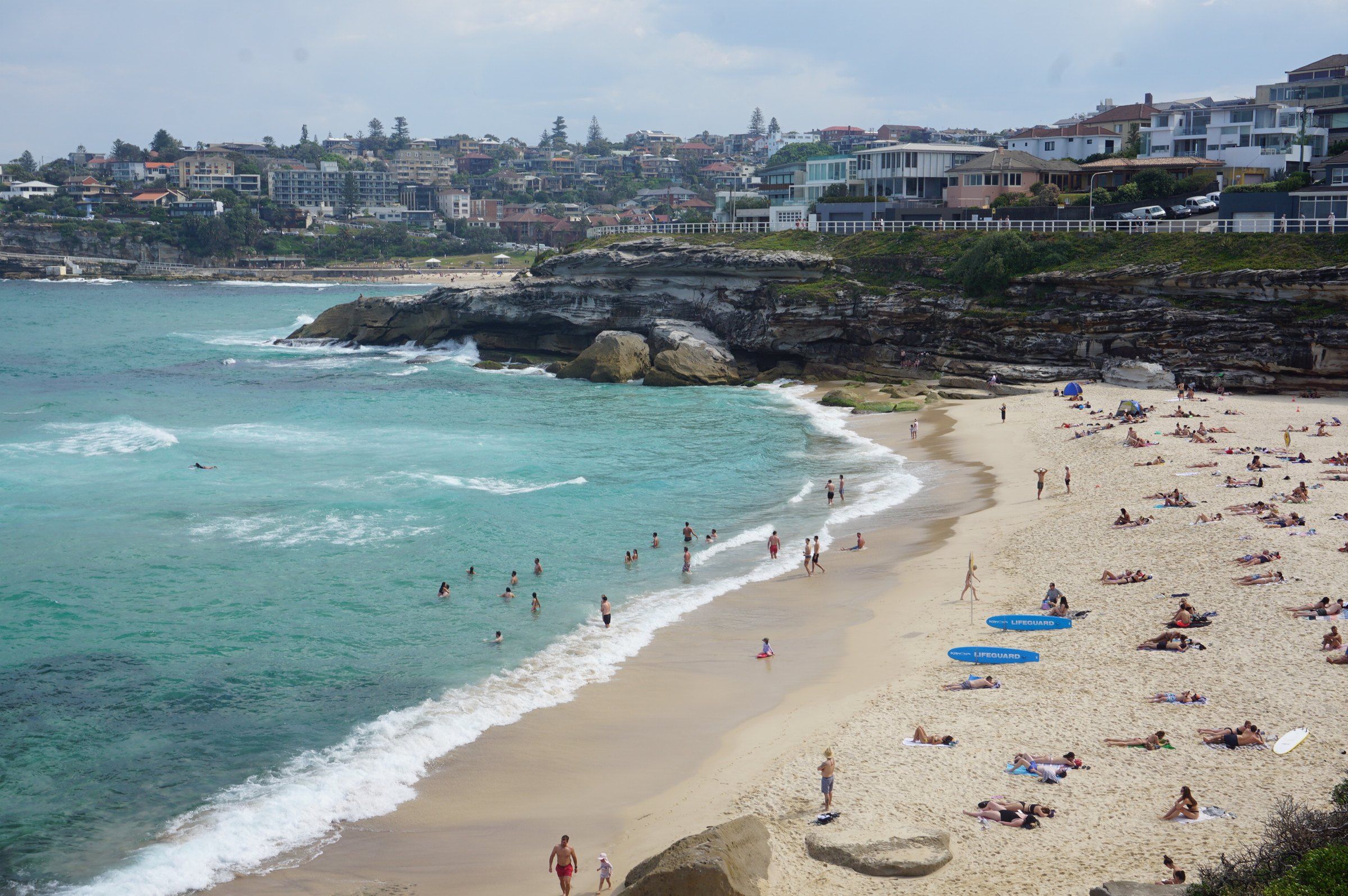 Swimmers and sunbathers on Tamarama Beach on a sunny day, houses on the cliffs behind