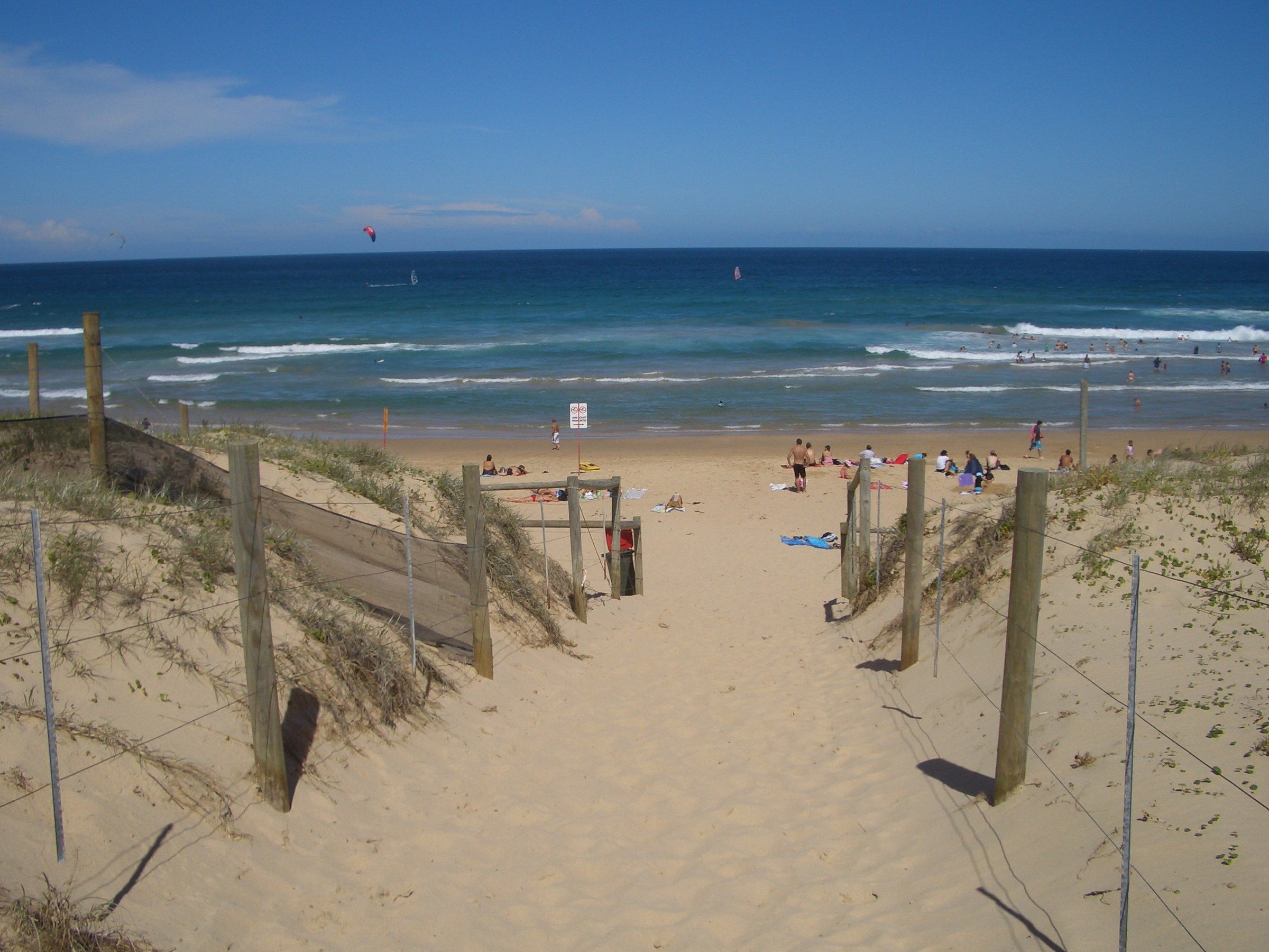 A sandy track between fences through the dunes onto Wanda Beach, the sea beyond