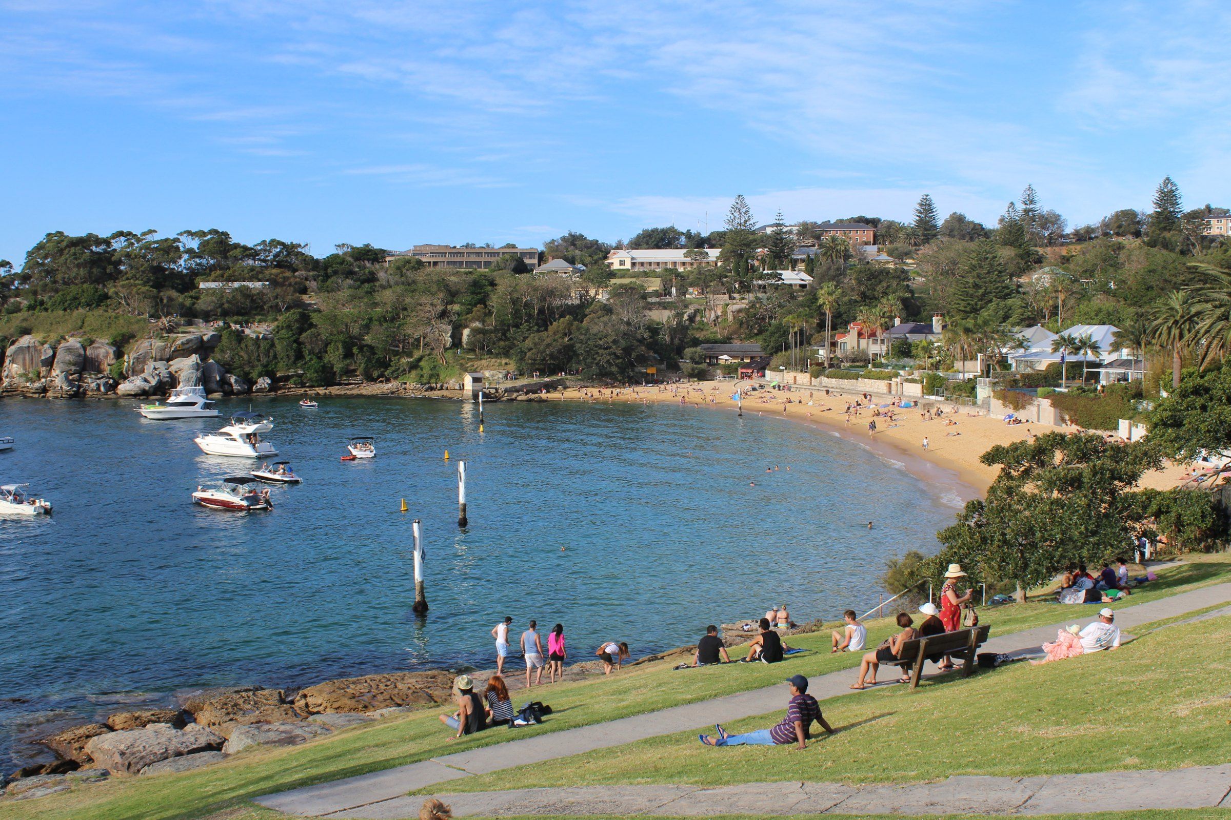 Camp Cove at Watsons Bay on a sunny day, boats moored in the calm harbour water and people on the grass